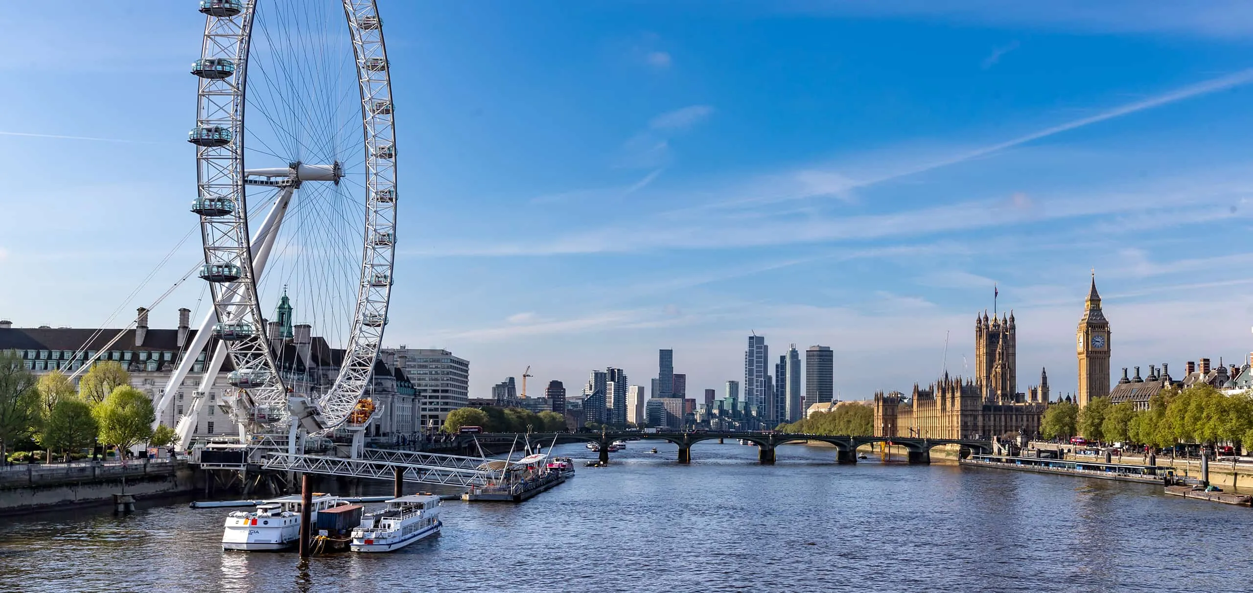 The London Eye with blue skies and the River Thames in the foreground