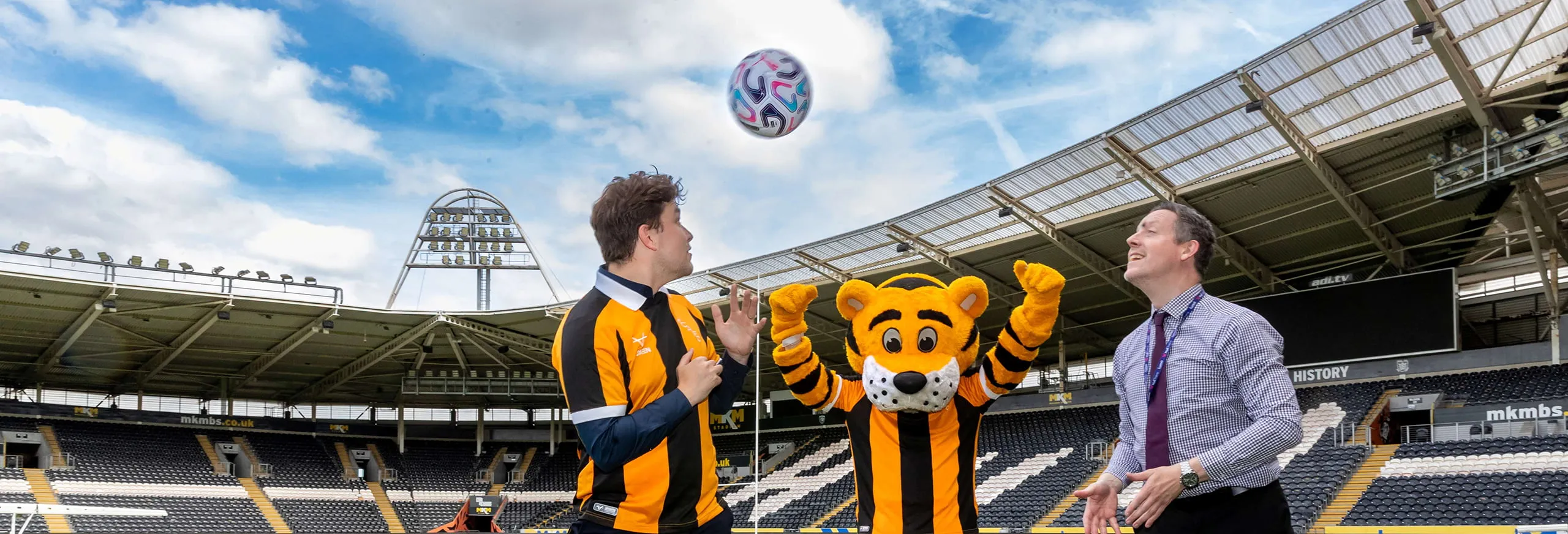 Two people and the Hull City mascot with a football in a stadium