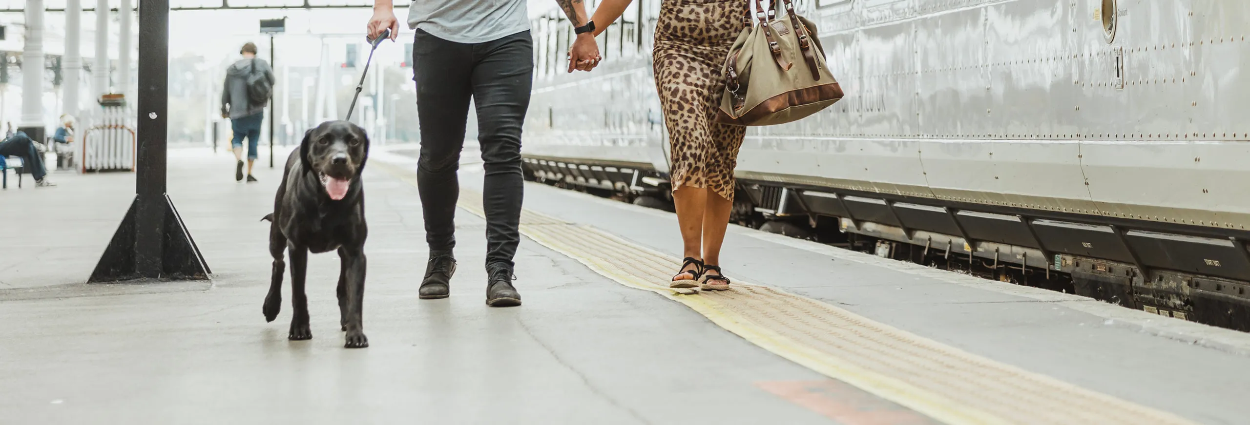 2 people with a dog on a lead in a train station