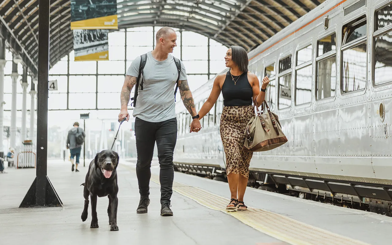 Two people with a dog on a lead in a train station